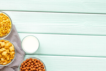 Various corn cereals in bowls and milk on mint wooden background top view copyspace