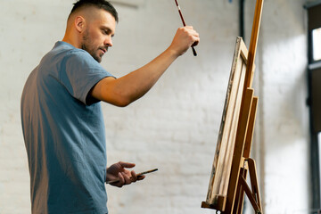 close-up in an art workshop an artist in a blue T-shirt actively paints with a brush on canvas