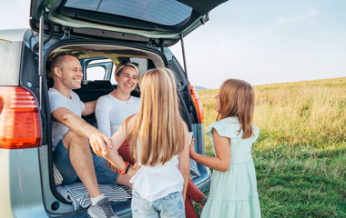 Portrait of Happy young couple with little daughters sitting inside car trunk during auto trop. They are smiling, laughing and chatting. Family values, traveling concept. © Soloviova Liudmyla