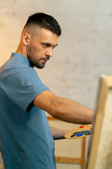 close up in an art workshop an artist in a blue T-shirt makes a wide stroke with a palette knife