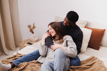 Positive diverse couple in casual clothes relaxing on bed at home 