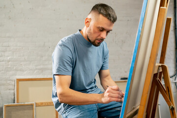Fototapeta premium young artist in a blue t-shirt in an art studio working on painting while sitting