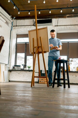 general shot young artist in a blue t-shirt in an art studio working on painting while