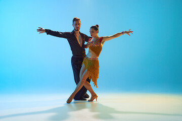 Elegant young man and woman, ballroom, Latin, samba dancers performing against gradient blue...