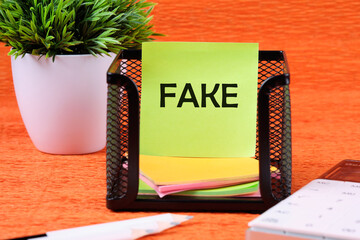 FAKE word written on a green sticker next to office supplies on an orange background
