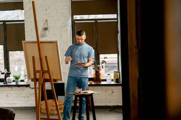general shot young artist in a blue t-shirt in an art studio working on painting