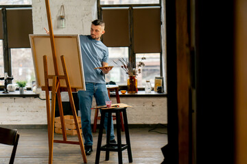 general shot young artist in a blue t-shirt in an art studio working on painting