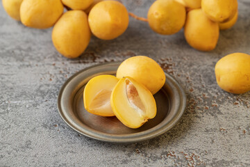 Ripe fresh yellow sliced dates on retro plate on grey vintage background.