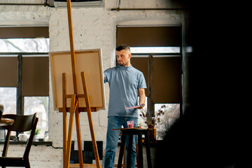 general shot young artist in a blue t-shirt in an art studio working on painting