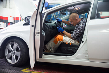 Canadian car service man worker in uniform adjusting steering wheel in car at car service
