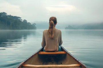 Muurstickers Rear view of woman sitting in a canoe in the middle of a large calm natural lake © Kien