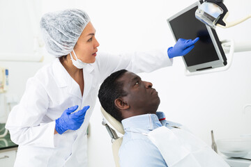 Confident asian female stomatologist showing teeth radiography result on computer screen to african...