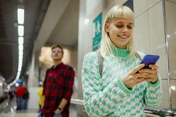 Smiling woman commuting to work by a train or a subway while using a phone