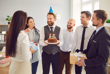 Happy colleagues gather in the office to celebrate a birthday and an anniversary party. Group surprises colleague with a birthday cake and gifts, making it a celebration in the workplace.