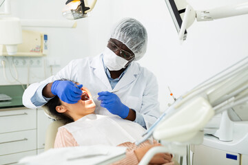 Professional african american dentist performing teeth treatment to adult woman in dental clinic..