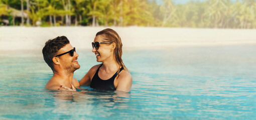 happy couple in love swimming in the ocean by tropical white sand beach. romantic getaway. banner...