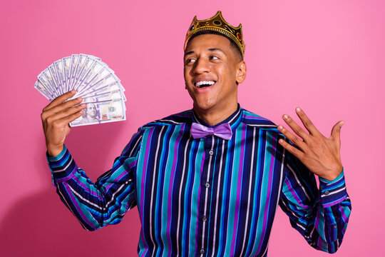 Photo of impressed funky guy wear striped shirt golden crown showing dollars fan isolated pink color background
