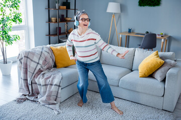 Full length photo of carefree positive grandmother have good mood dancing listen music apartment...