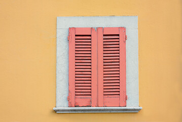 yellow house facade and window with closed red shutters, exfoliated paint