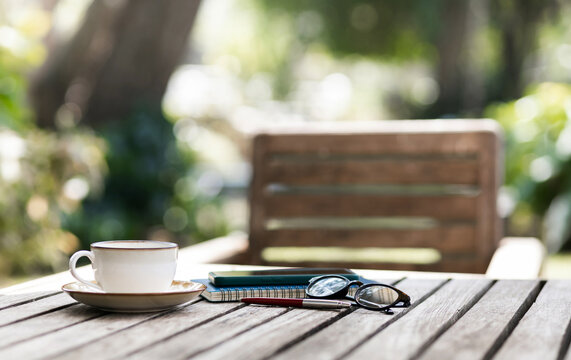 White coffee cup with mobile and note book on old wooden table in outdoor garden
