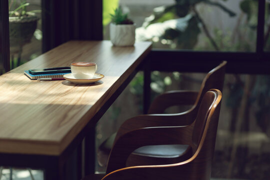 Latte coffee with mobile and note book on wooden counter with seat in cafe and outdoor garden background
