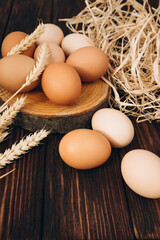 Chicken eggs of different brown and beige shades on a wooden background with dry corn and wheat. Easter background. Top view