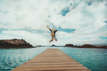Happy man traveler jumping from a jetty into a lake on a sunny day - Delightful tourist enjoying summertime vacation  - obrazy, fototapety, plakaty