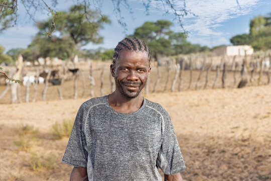 african man with braids , in the village, standing in front of the kraal with small livestock