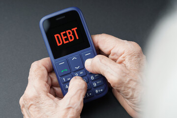 The concept of debts to old ages. Old wrinkled hands holding phone on which the debt message arrived.