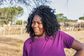 african woman with braids , in the village, standing in front of the kraal with small livestock