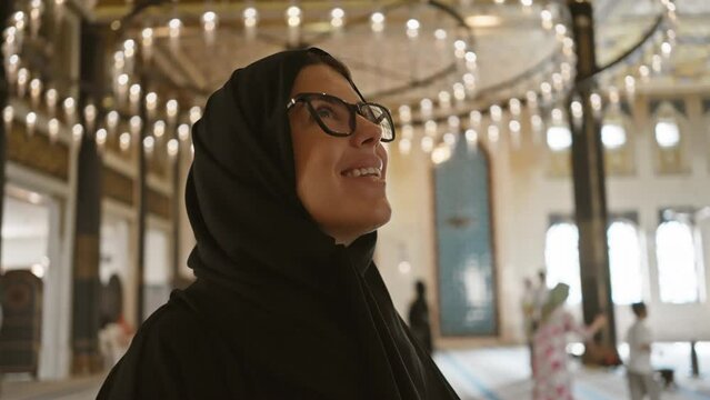 A smiling woman in glasses and hijab inside the ornate architecture of katara cultural village mosque in doha, qatar