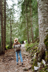 Naklejka na ściany i meble Young woman with backpack walking in beautiful forest. Hiking and leisure theme.