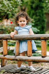 Curious child exploring nature, standing by a wooden fence in a lush green garden