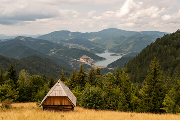 Cottage surrounded by forest high in the mountain with view on the lake, Zaovine, Tara, Serbia - obrazy, fototapety, plakaty