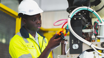 An African professional engineering is fixing or testing the arm of robotic that use in the factory...