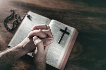 Hands folded in prayer on a Holy Bible in church, faith, spirtuality and religion