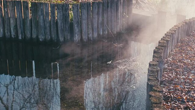 Fog, steam and sun on the water from natural pool with wooden bards
