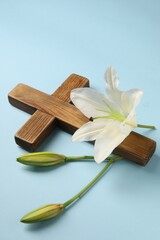 Wooden cross and lily flowers on light blue background. Easter attributes