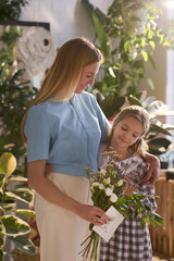 Vertical medium long shot of happy mother and daughter posing for camera on Mothers day in room with biophilic design