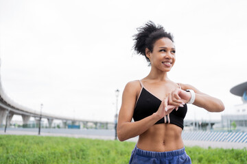 Naklejka premium Athletic woman checking fitness tracker after a workout, with an urban landscape in the background.