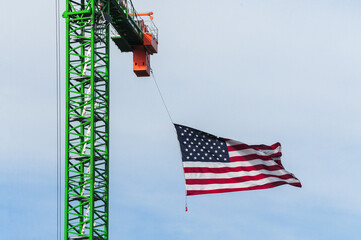 American flag suspended from a green tower crane against blue sky, illustrating patriotic display at commercial construction site and symbolic integration of national pride in building projects