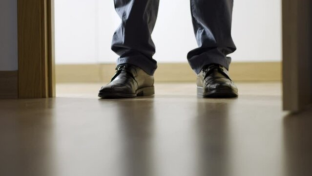 Cropped shot of male legs taking off shoes to not make noise and walking barefoot on warm wooden floor in living room at home, heating concept