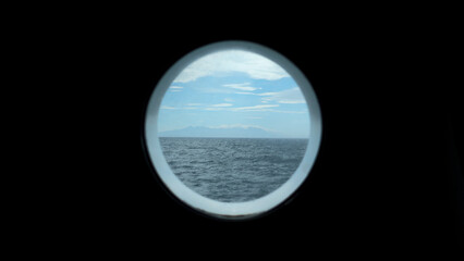 View from round deck window to sea. Clip. Beautiful seascape with mountain coast on horizon from round window. Sea voyage and view from round window