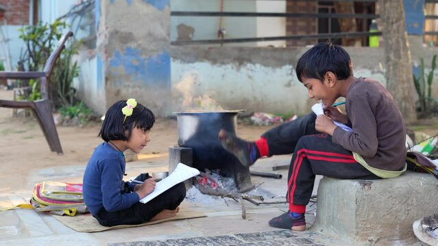 Elementary school students girl and boy doing homework outdoor. Village kids reading book and writing with pencil. Poor children education learning studying together