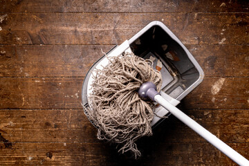 floor cleaning mop in a grey mop bucket on a wooden floor