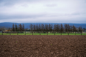 Freshly plowed field with a fenced paddock behind it