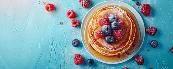 A stack of fluffy pancakes with maple syrup and berries. Top down view on a vibrant blue background...