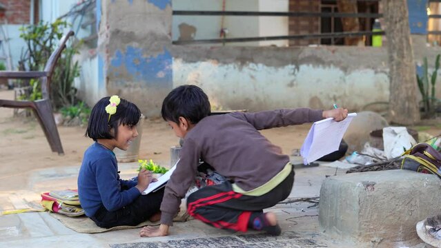 Two cute teenager student sister and brother, are doing together homework sitting after school in the garden, Brother is helping and explaining the other one the task