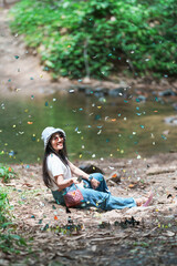 Lifestyle, Asian Woman travel on vacation. Ecotourism adventure, explore nature butterfly in forest. She is sitting riverside relax happy, among colorful butterflies flying. Kaeng Krachan, Thailand.