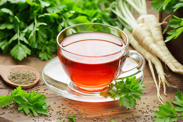 Parsley tea with fresh seeds, leaves, roots nearby on rustic wooden table, copy space, natural...
